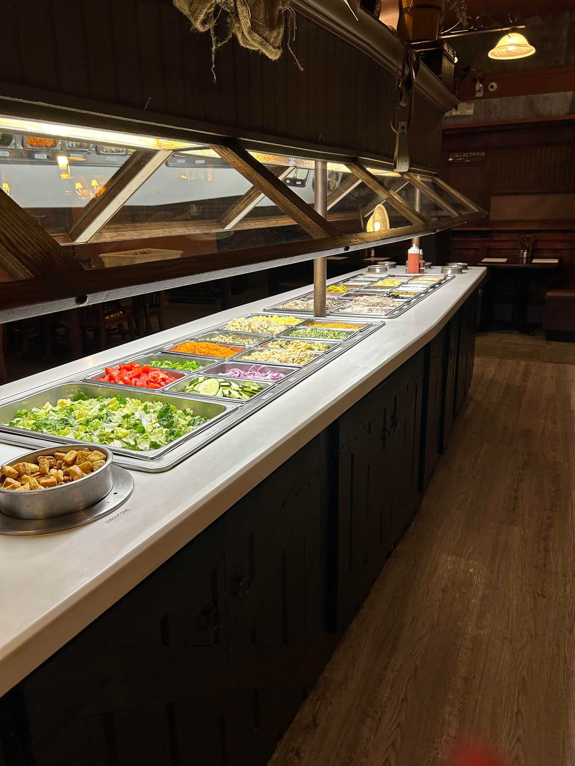Buffet salad bar with a variety of fresh vegetables and toppings in a rustic restaurant setting.