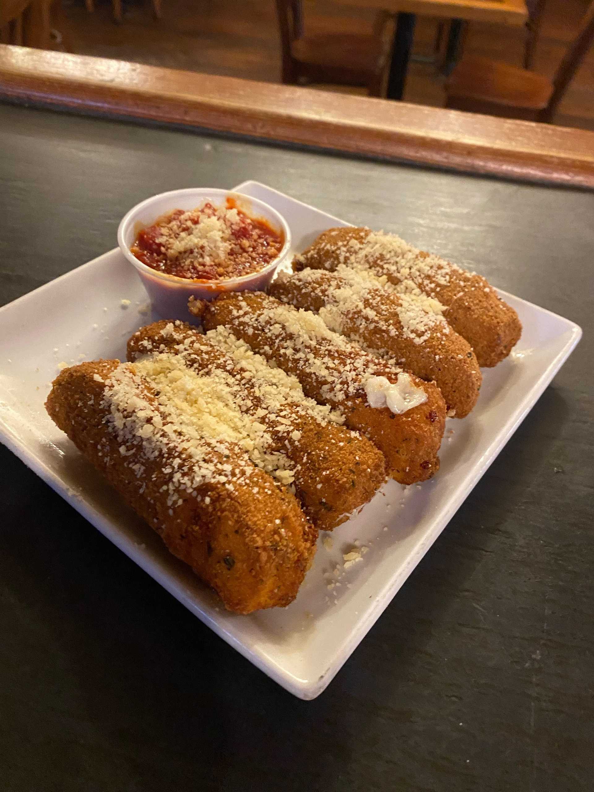 Plate of breadsticks covered in cheese with marinara sauce on the side.