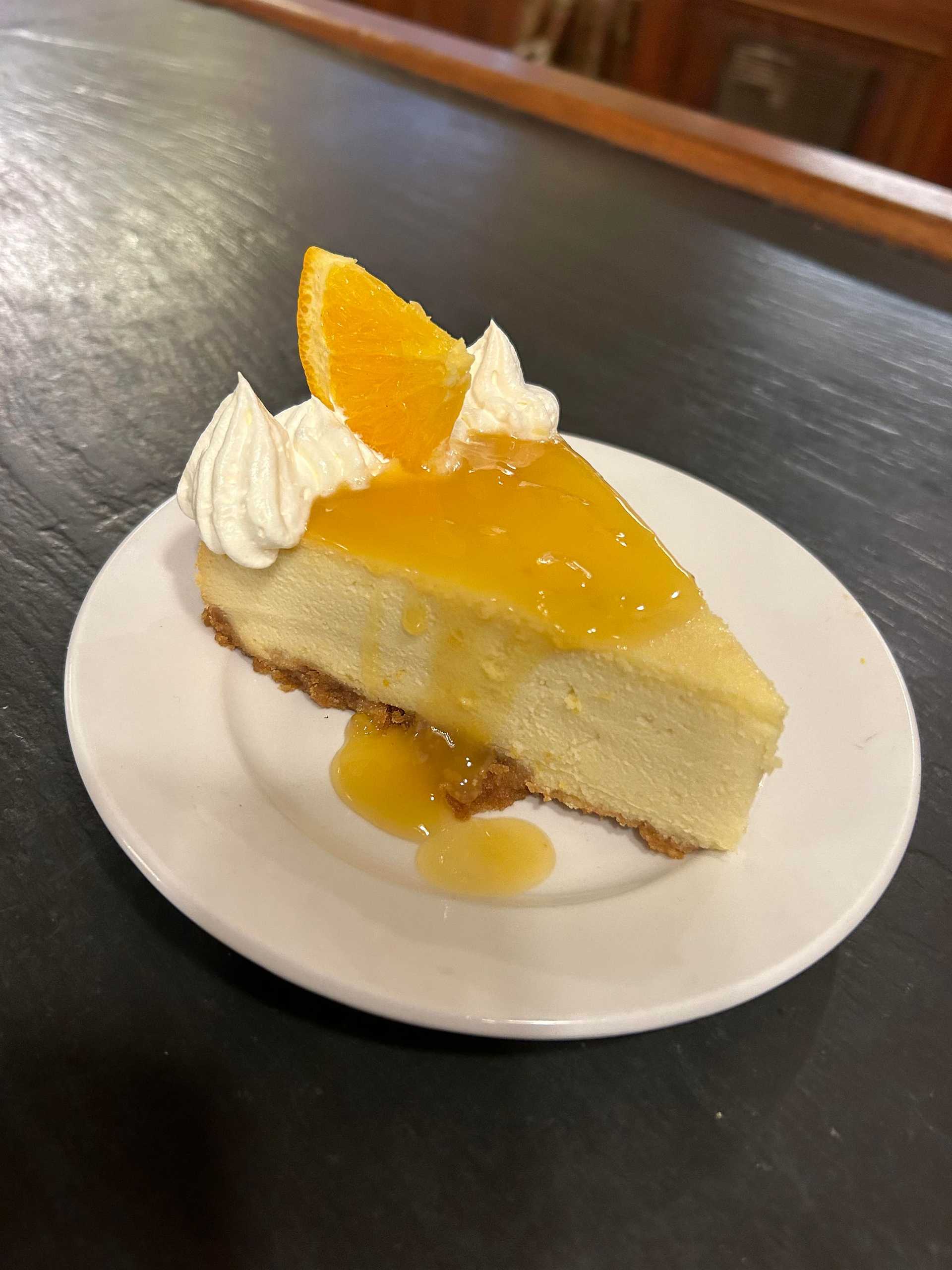 Slice of cheesecake with orange glaze, whipped cream, and a fresh orange slice on top.